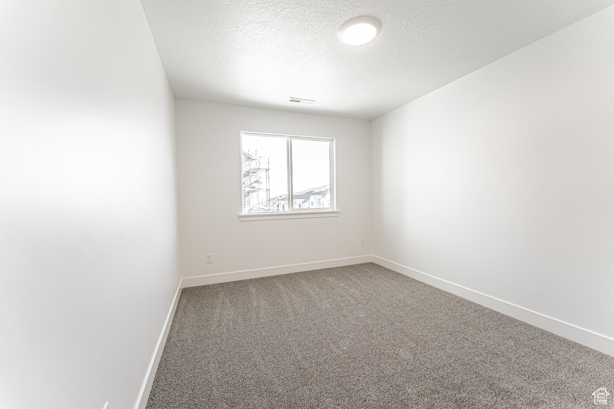 Carpeted spare room featuring baseboards, visible vents, and a textured ceiling