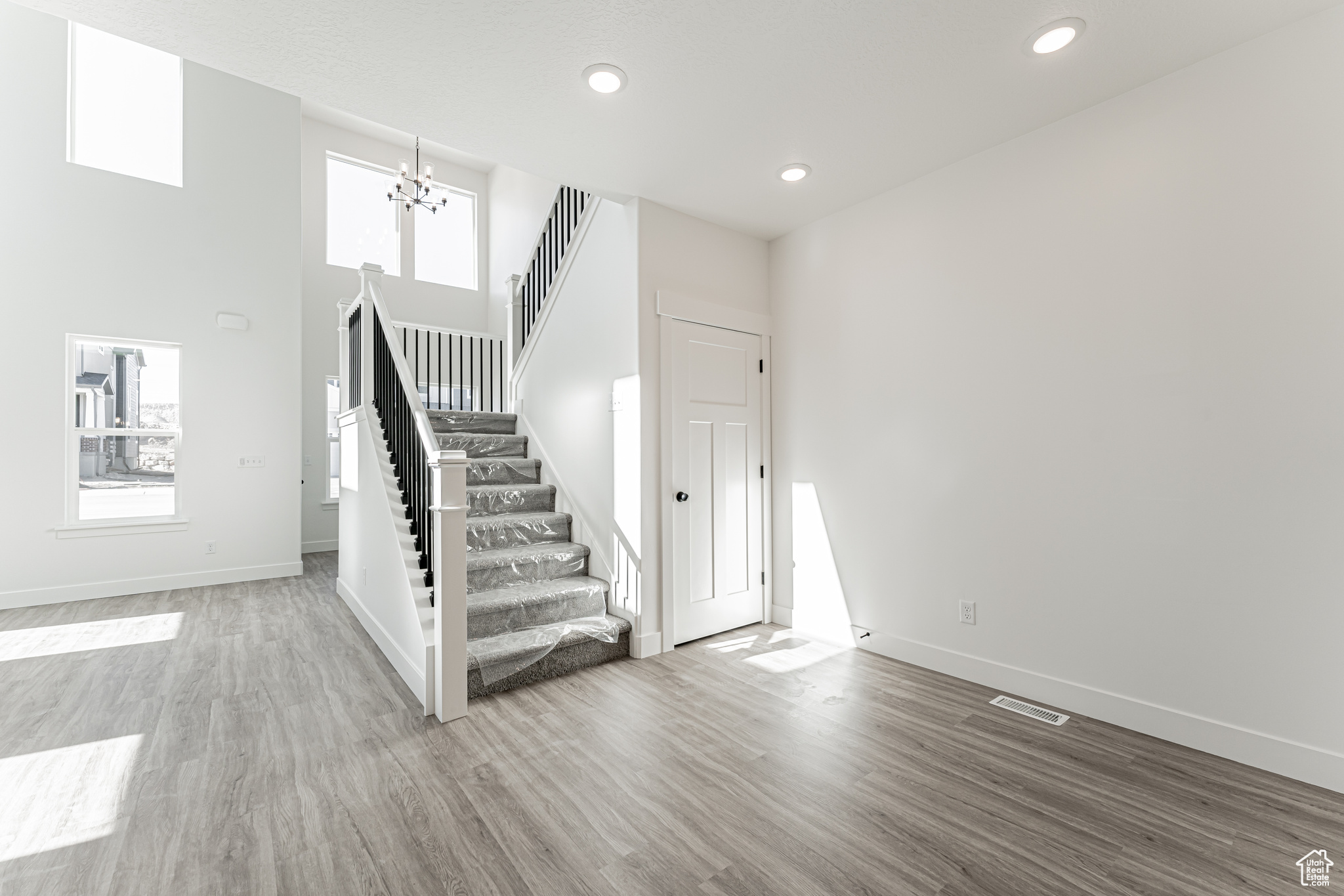 Stairs with a notable chandelier, a healthy amount of sunlight, baseboards, and wood finished floors