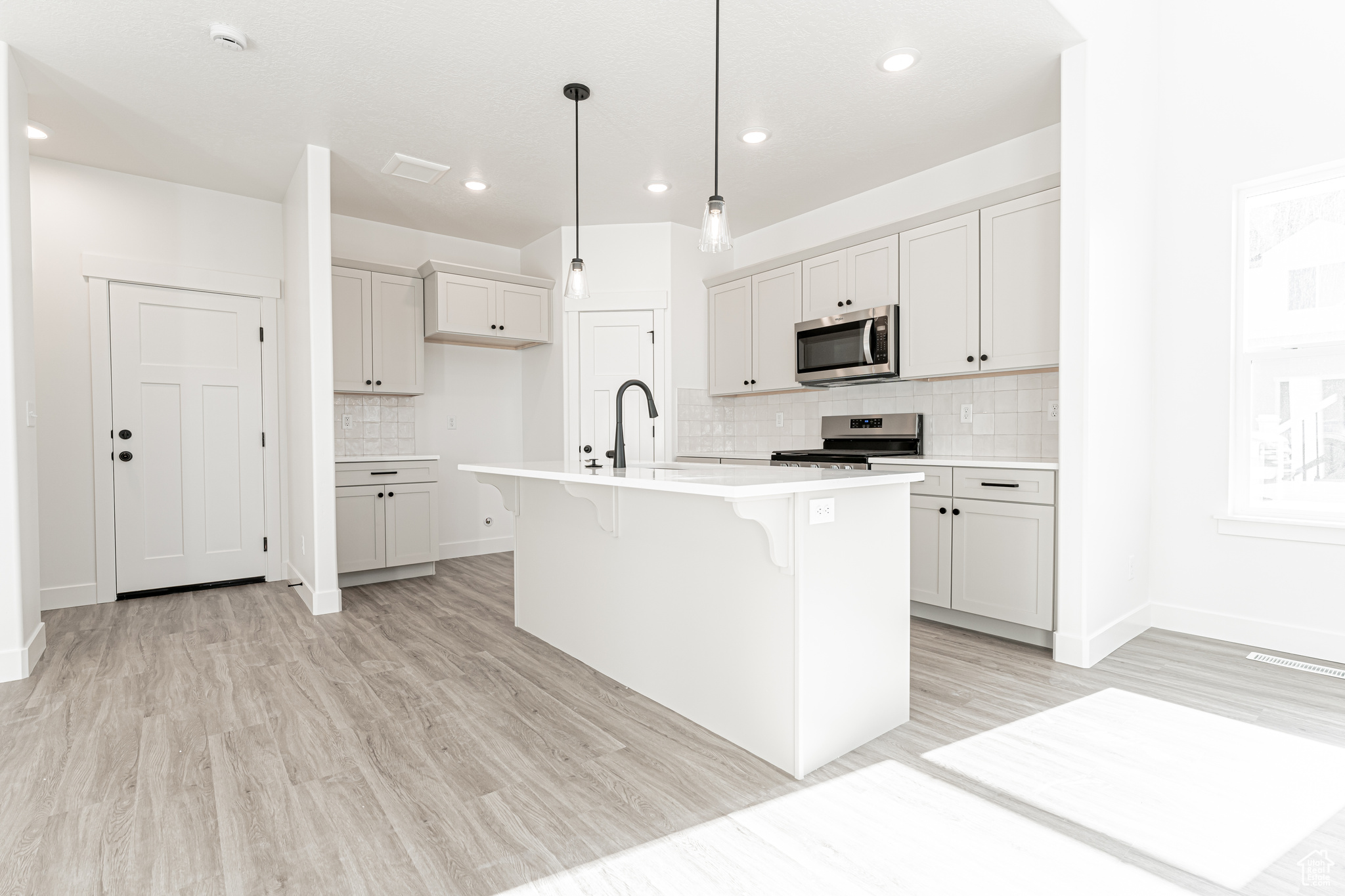 Kitchen with an island with sink, decorative backsplash, light countertops, appliances with stainless steel finishes, and a kitchen bar