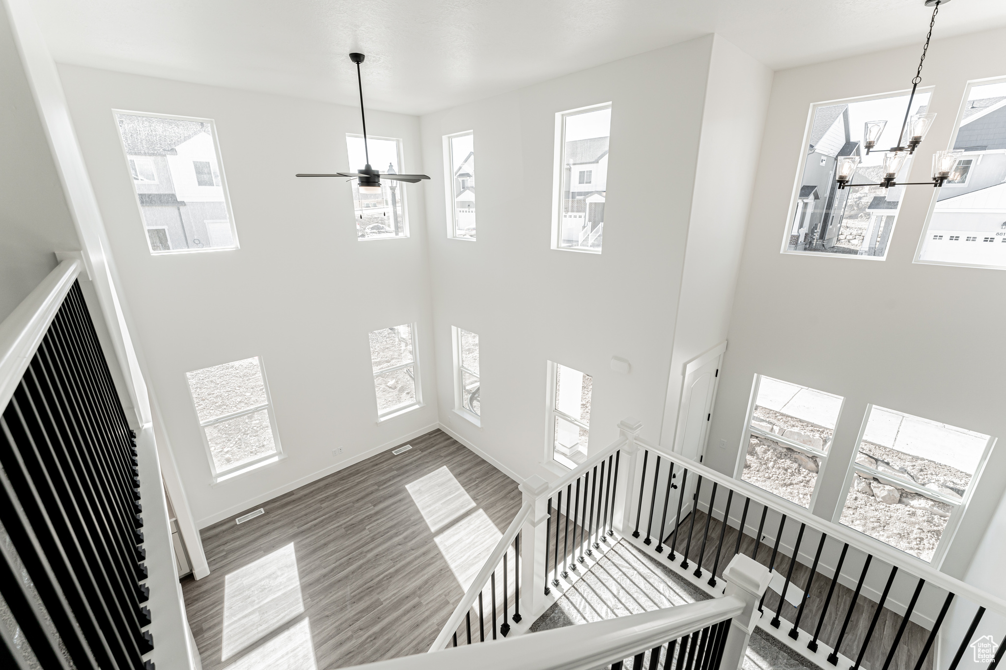 Staircase featuring ceiling fan with notable chandelier, a high ceiling, baseboards, and wood finished floors