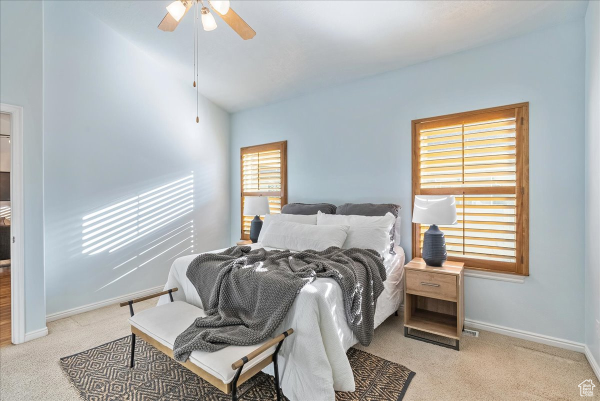 Bedroom with light carpet, multiple windows, and ceiling fan