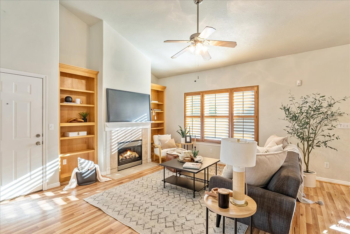 Living room with lofted ceiling, a tiled fireplace, hardwood / wood-style flooring, and ceiling fan