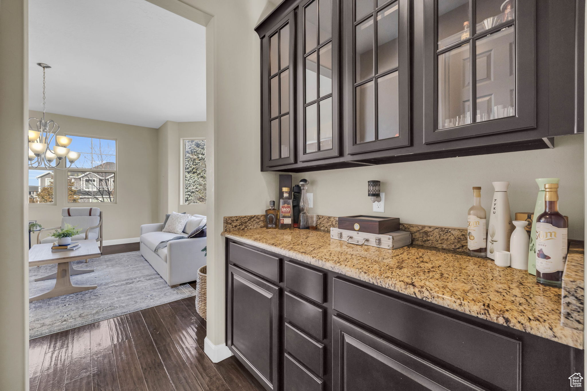 Bar featuring dark brown cabinets, dark hardwood / wood-style flooring, light stone counters, and a notable chandelier