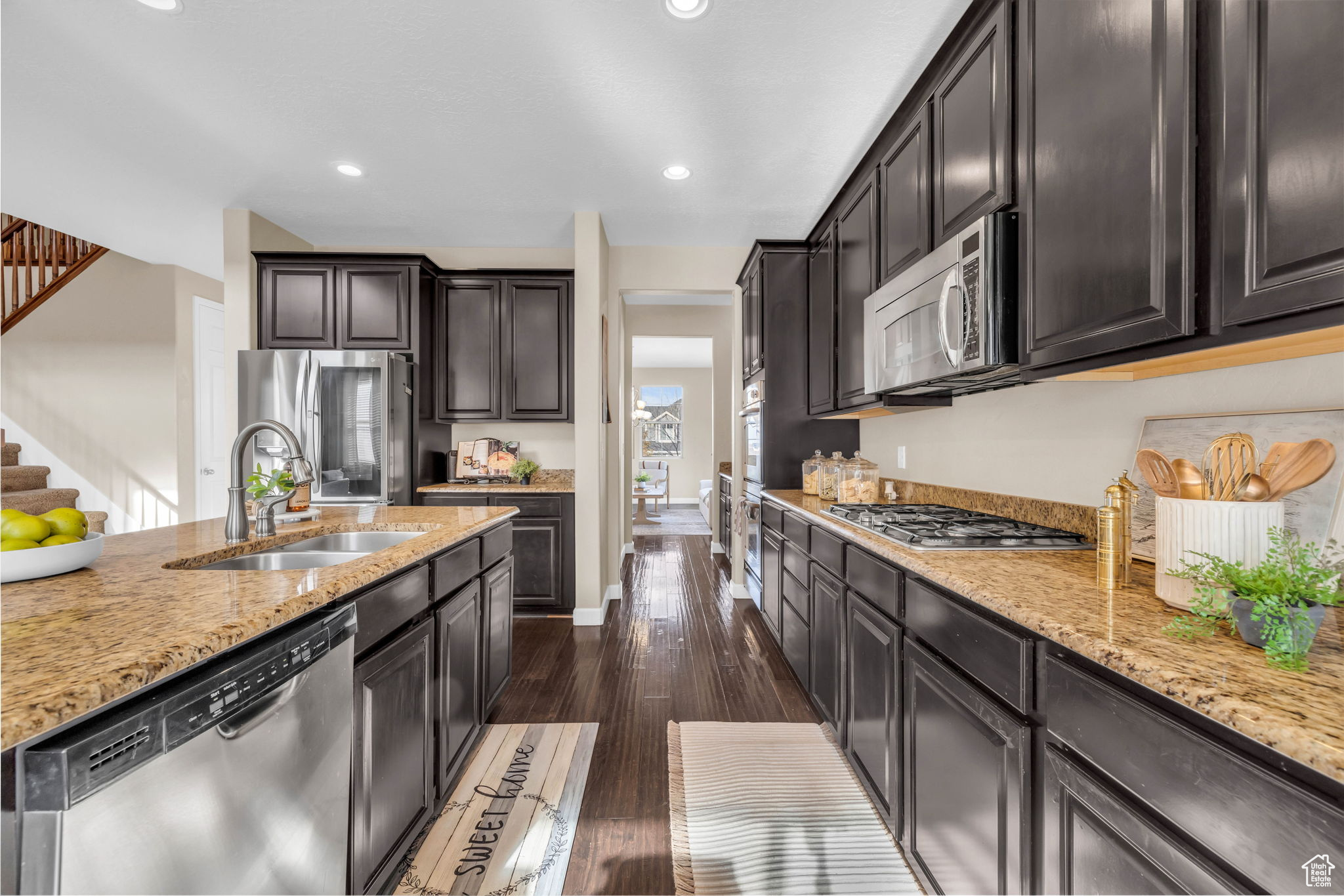 Kitchen featuring light stone counters, dark brown cabinetry, stainless steel appliances, dark wood-type flooring, and sink