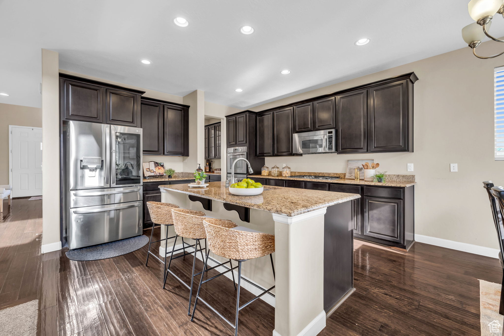 Kitchen featuring appliances with stainless steel finishes, dark hardwood / wood-style flooring, a breakfast bar, dark brown cabinetry, and a kitchen island with sink