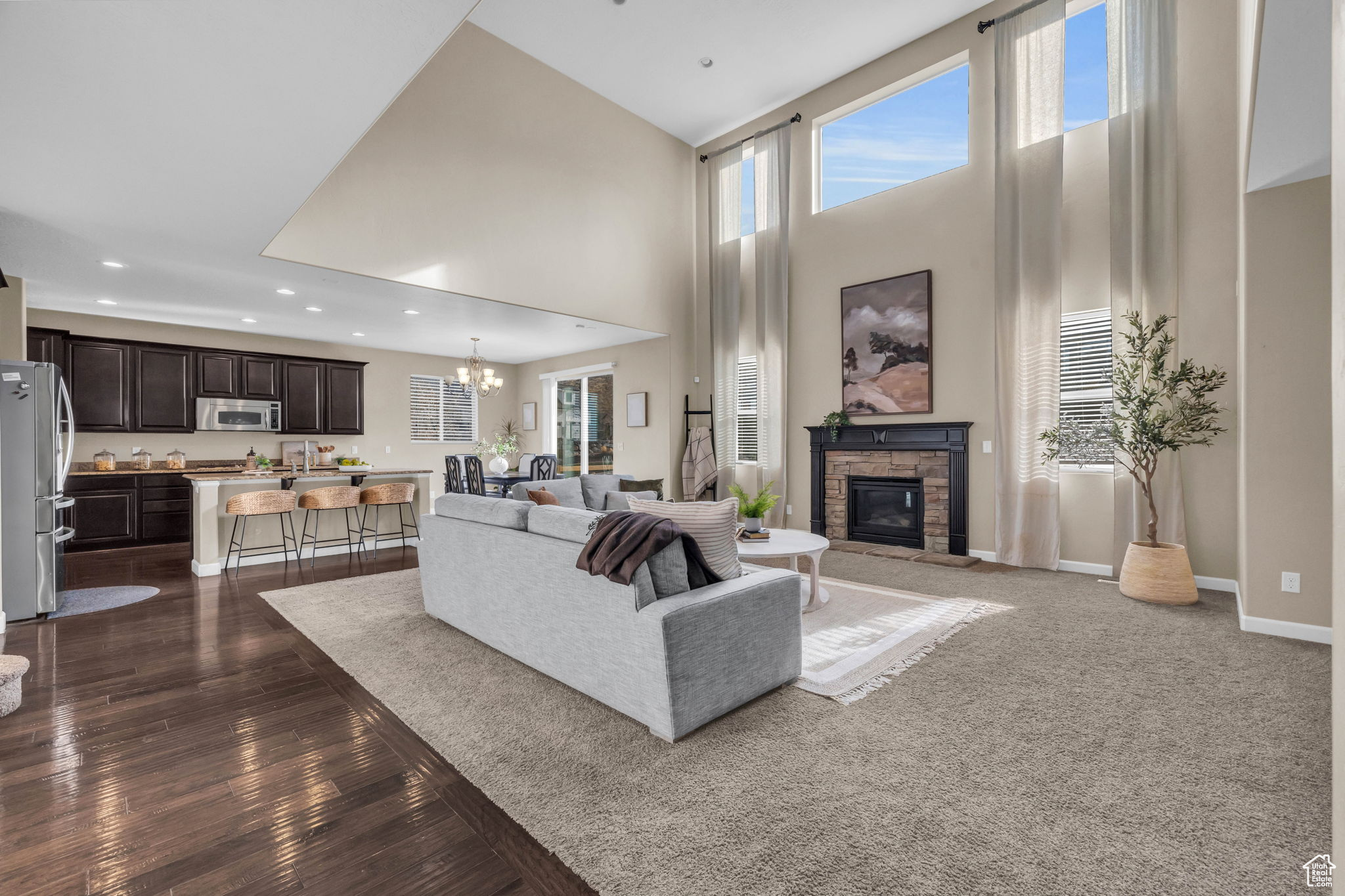 Living room featuring a stone fireplace, dark hardwood / wood-style floors, a high ceiling, and a notable chandelier