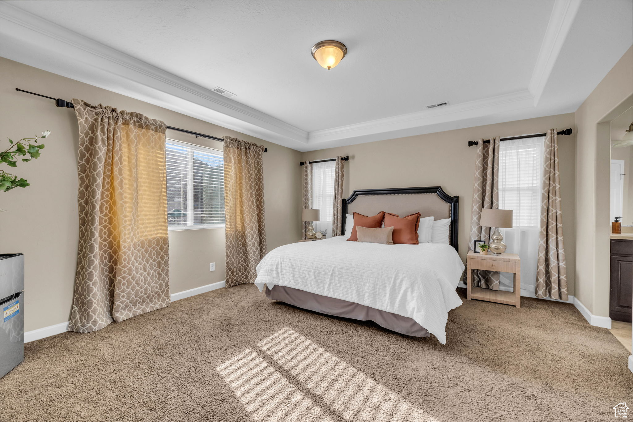 Bedroom with ornamental molding, light colored carpet, multiple windows, and a tray ceiling