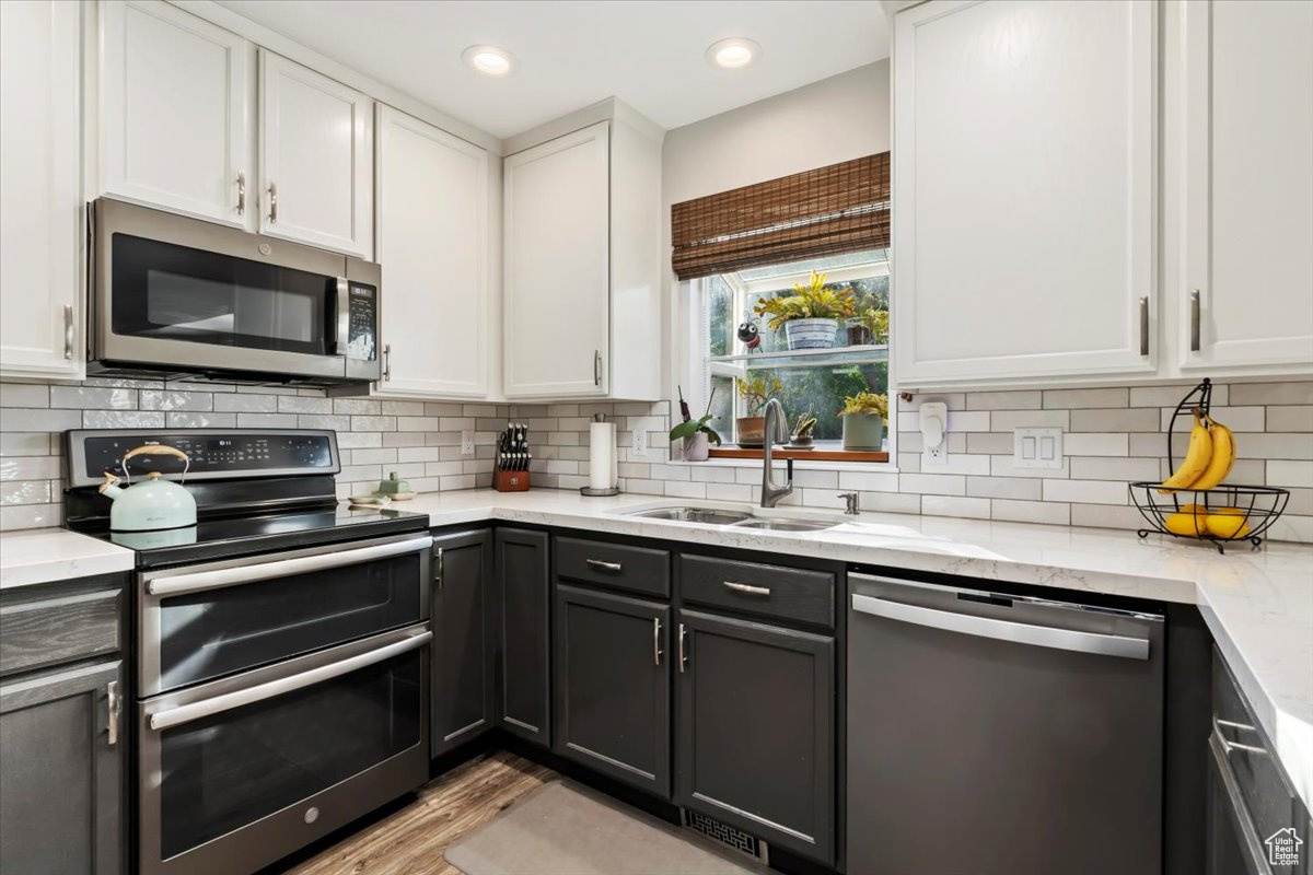 Kitchen featuring white cabinets, light stone counters, backsplash, sink, and stainless steel appliances