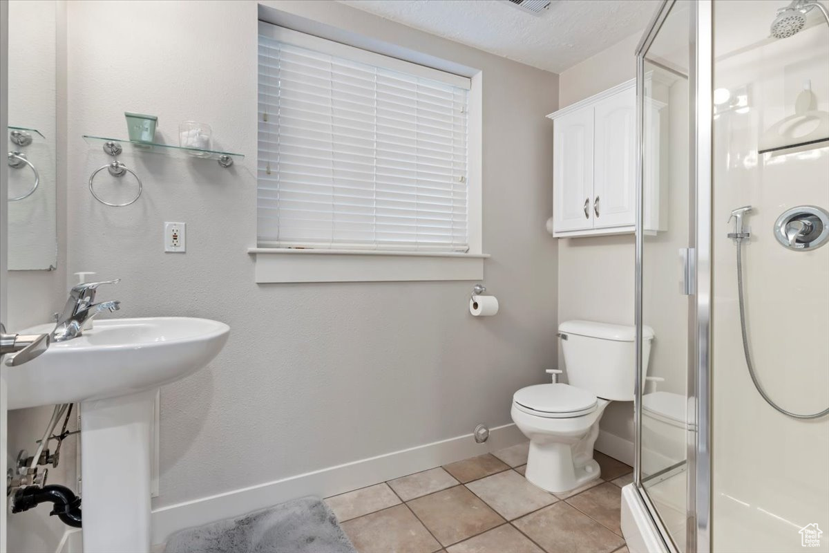 Bathroom with a shower with door, toilet, and tile patterned floors