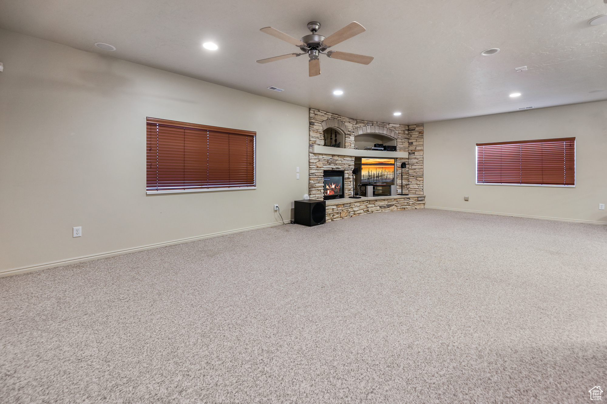 Unfurnished living room with a stone fireplace, carpet flooring, and ceiling fan