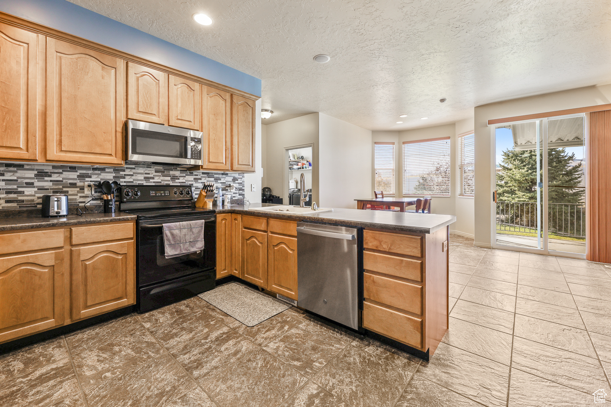 Kitchen featuring decorative backsplash, kitchen peninsula, stainless steel appliances, sink, and a textured ceiling