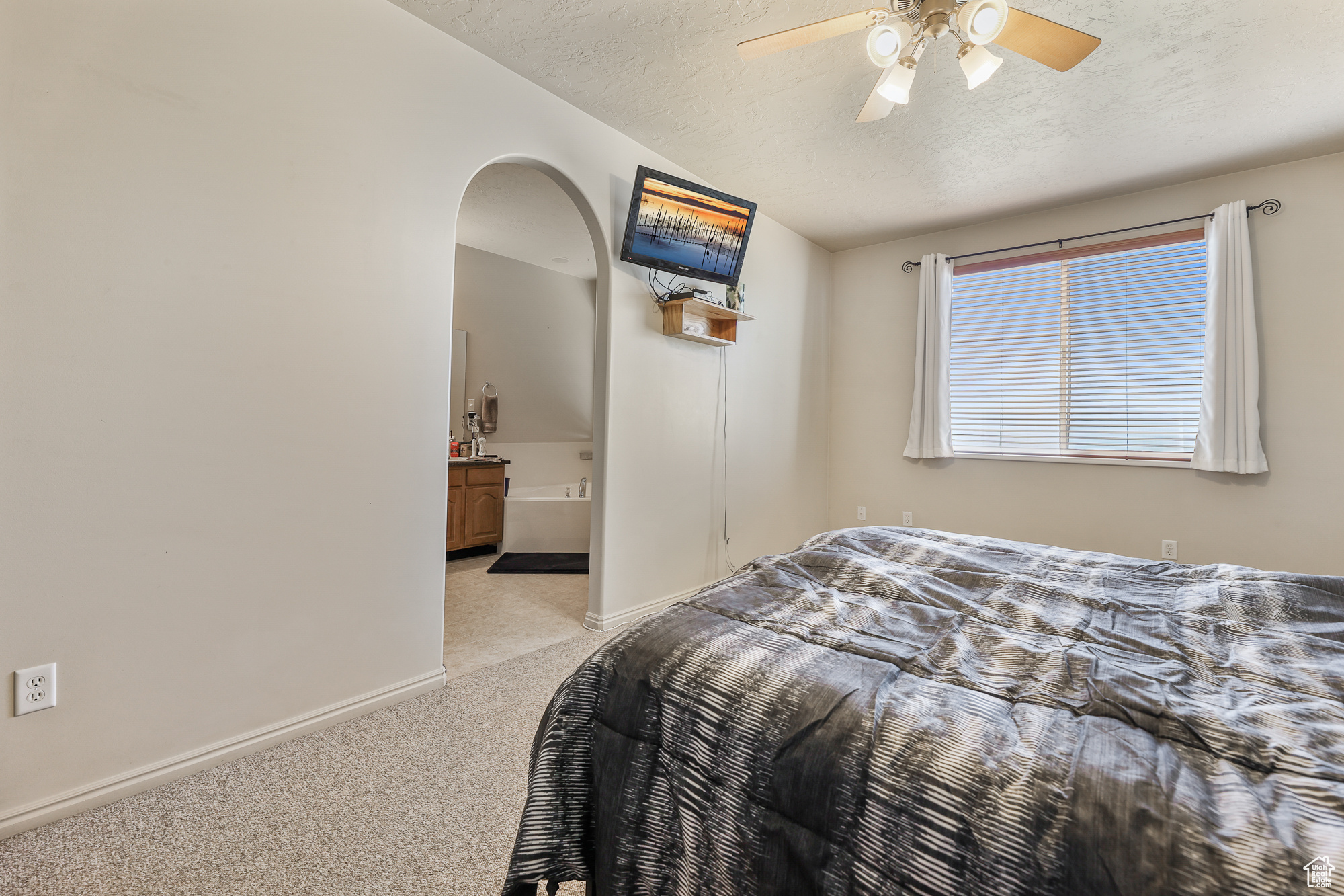 Carpeted bedroom with connected bathroom, ceiling fan, and a textured ceiling