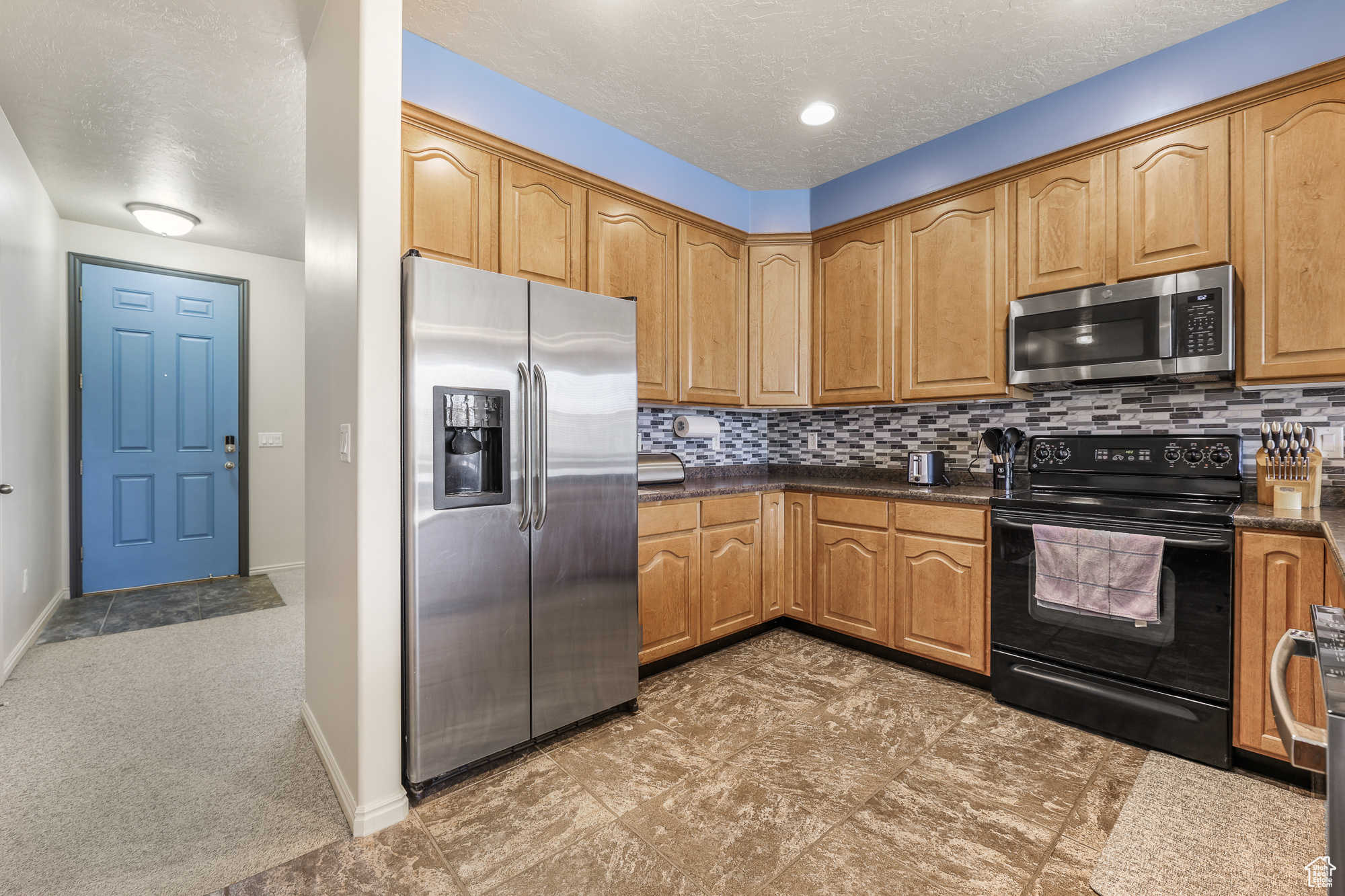 Kitchen with appliances with stainless steel finishes, a textured ceiling, and decorative backsplash