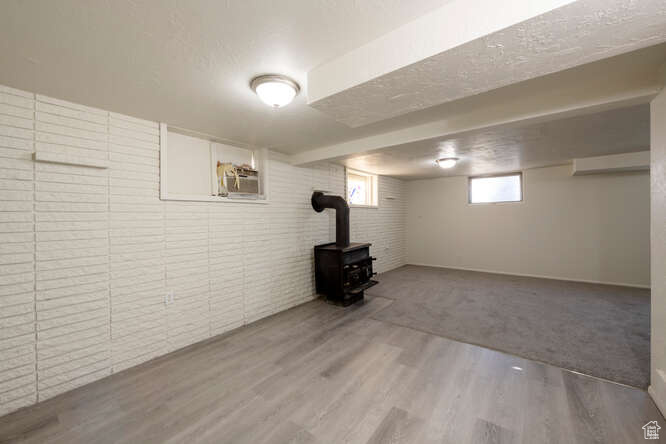 Basement with an AC wall unit, wood-type flooring, a textured ceiling, and a wood stove