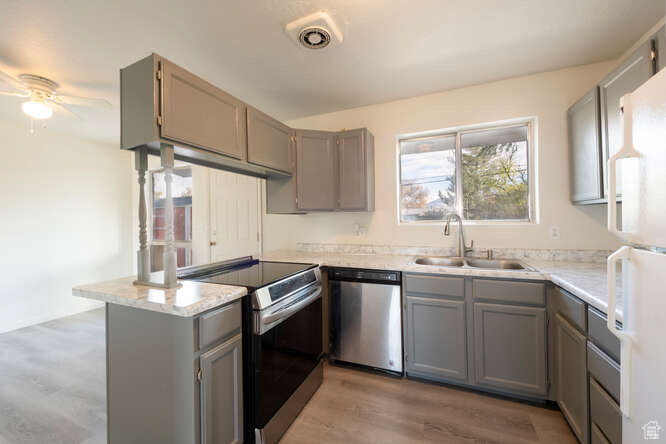 Kitchen with kitchen peninsula, wood-type laminate flooring, sink, gray cabinetry, and stainless steel appliances