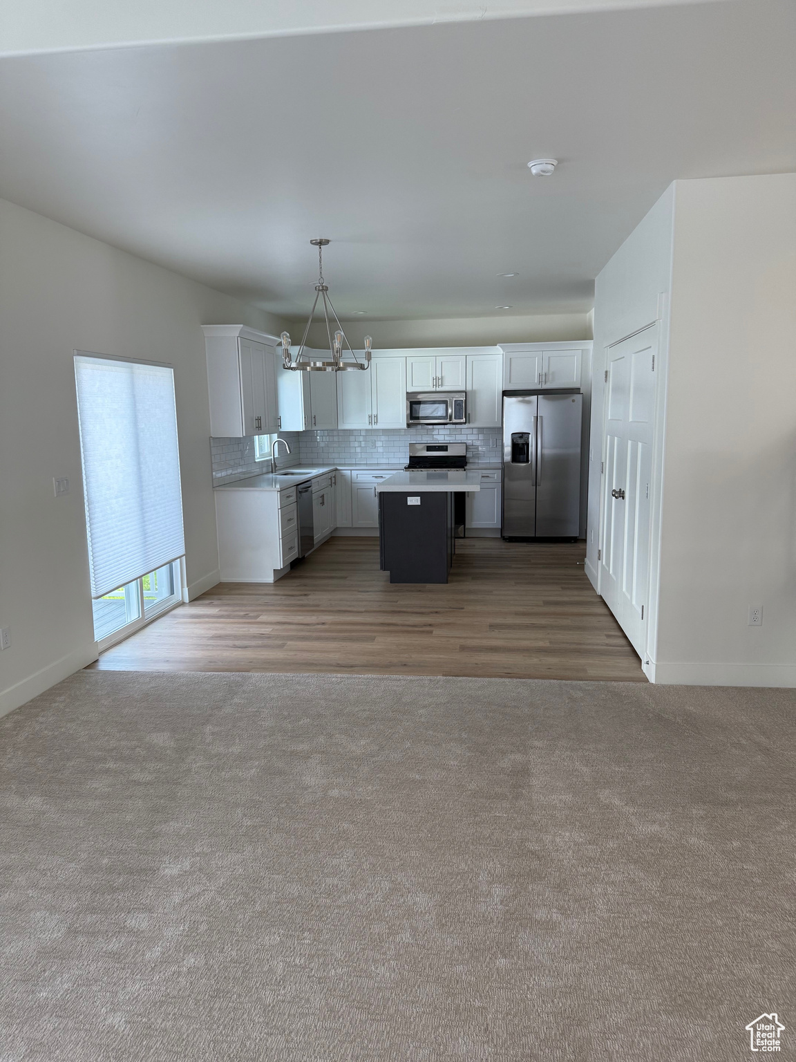 Kitchen with sink, a kitchen island, hanging light fixtures, white cabinetry, and stainless steel appliances