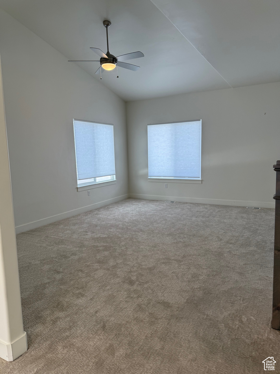 Carpeted empty room featuring vaulted ceiling and ceiling fan