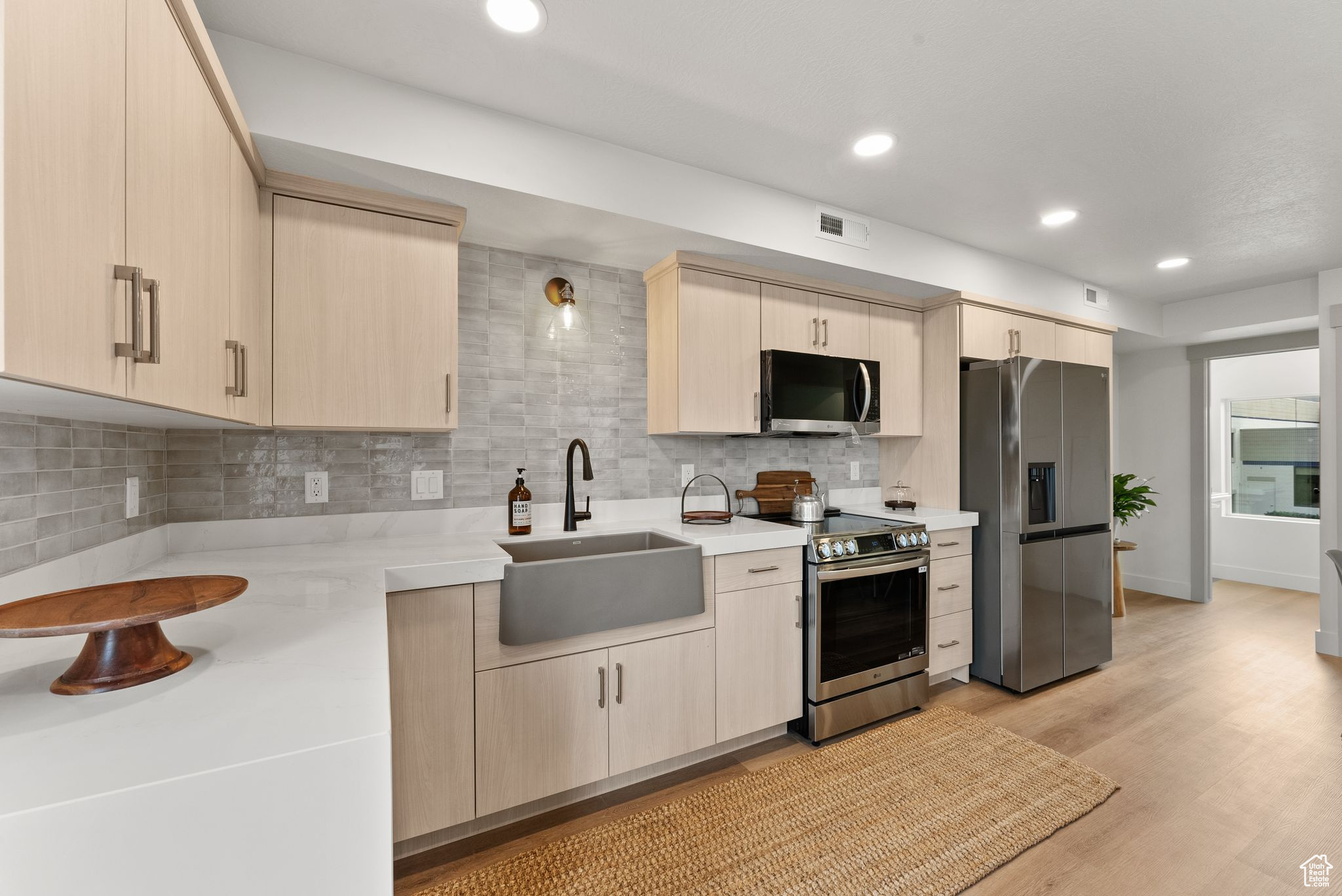 Kitchen featuring sink, tasteful backsplash, light wood-type flooring, light brown cabinetry, and appliances with stainless steel finishes