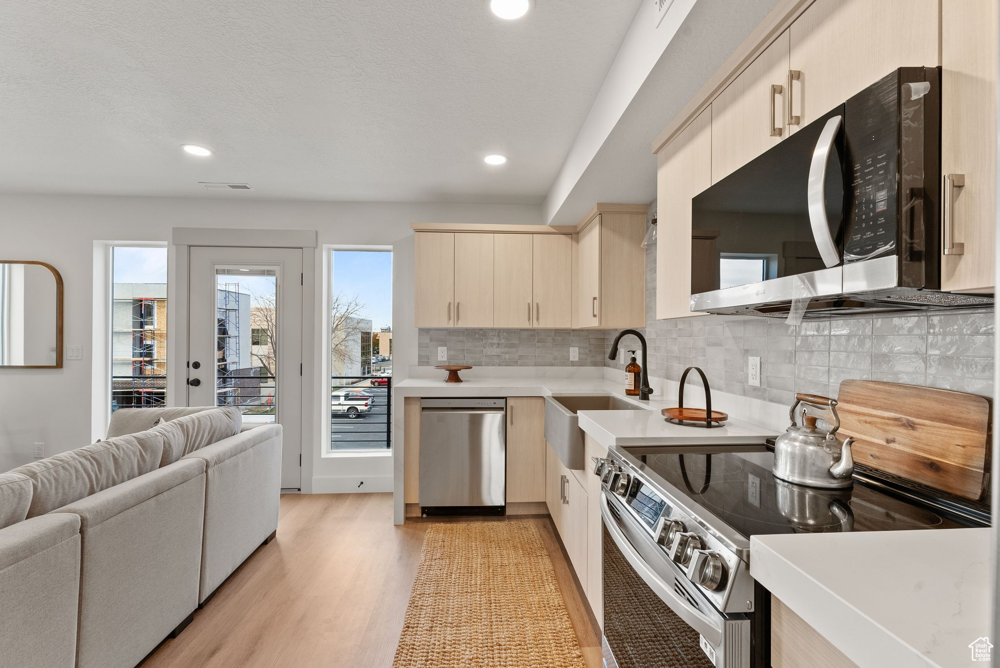 Kitchen featuring backsplash, cream cabinets, sink, appliances with stainless steel finishes, and light hardwood / wood-style floors