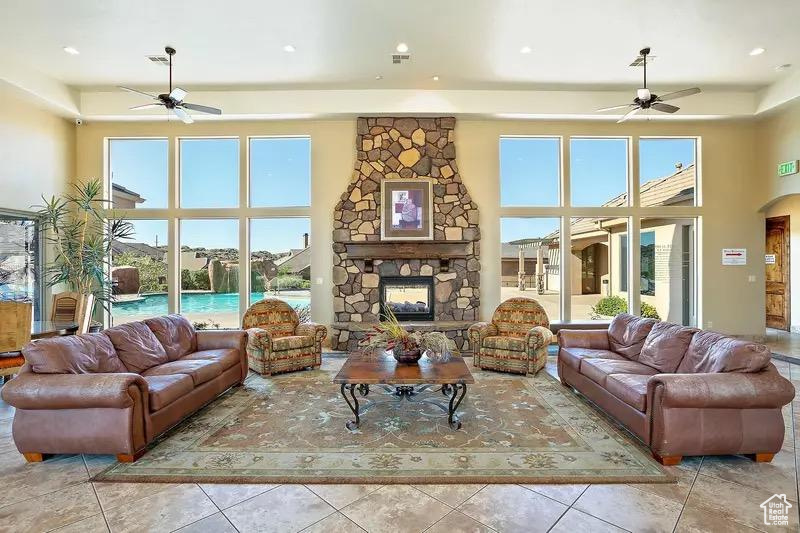 Tiled living room featuring ceiling fan, a stone fireplace, and a towering ceiling