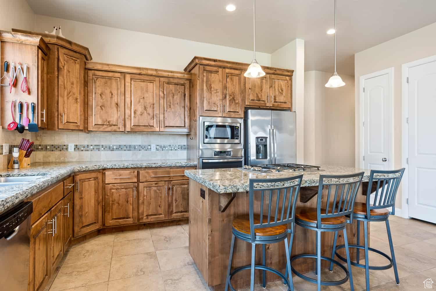 Kitchen featuring a kitchen island, stainless steel appliances, decorative light fixtures, light stone counters, and decorative backsplash