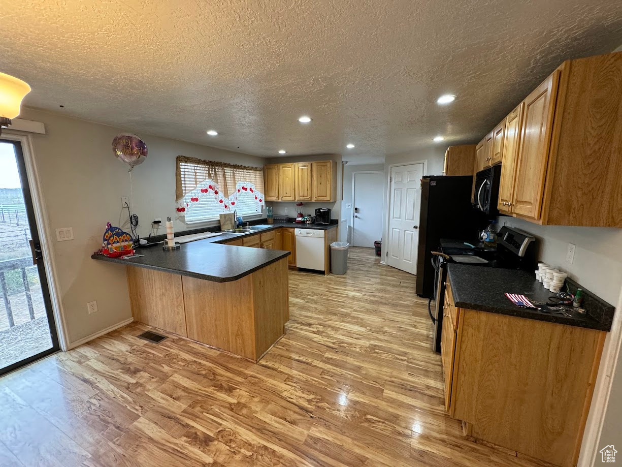 Kitchen with a peninsula, stainless steel electric stove, black microwave, dishwasher, and light wood-type flooring