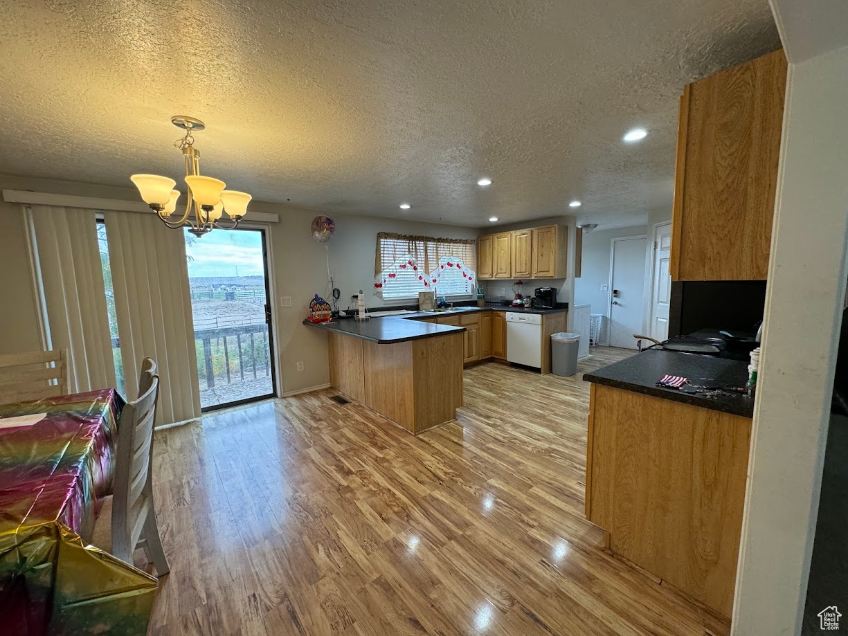 Kitchen with light wood-type flooring, dark countertops, a peninsula, an inviting chandelier, and white dishwasher