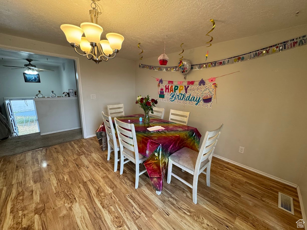 Dining room with visible vents, ceiling fan with notable chandelier, a textured ceiling, wood finished floors, and baseboards