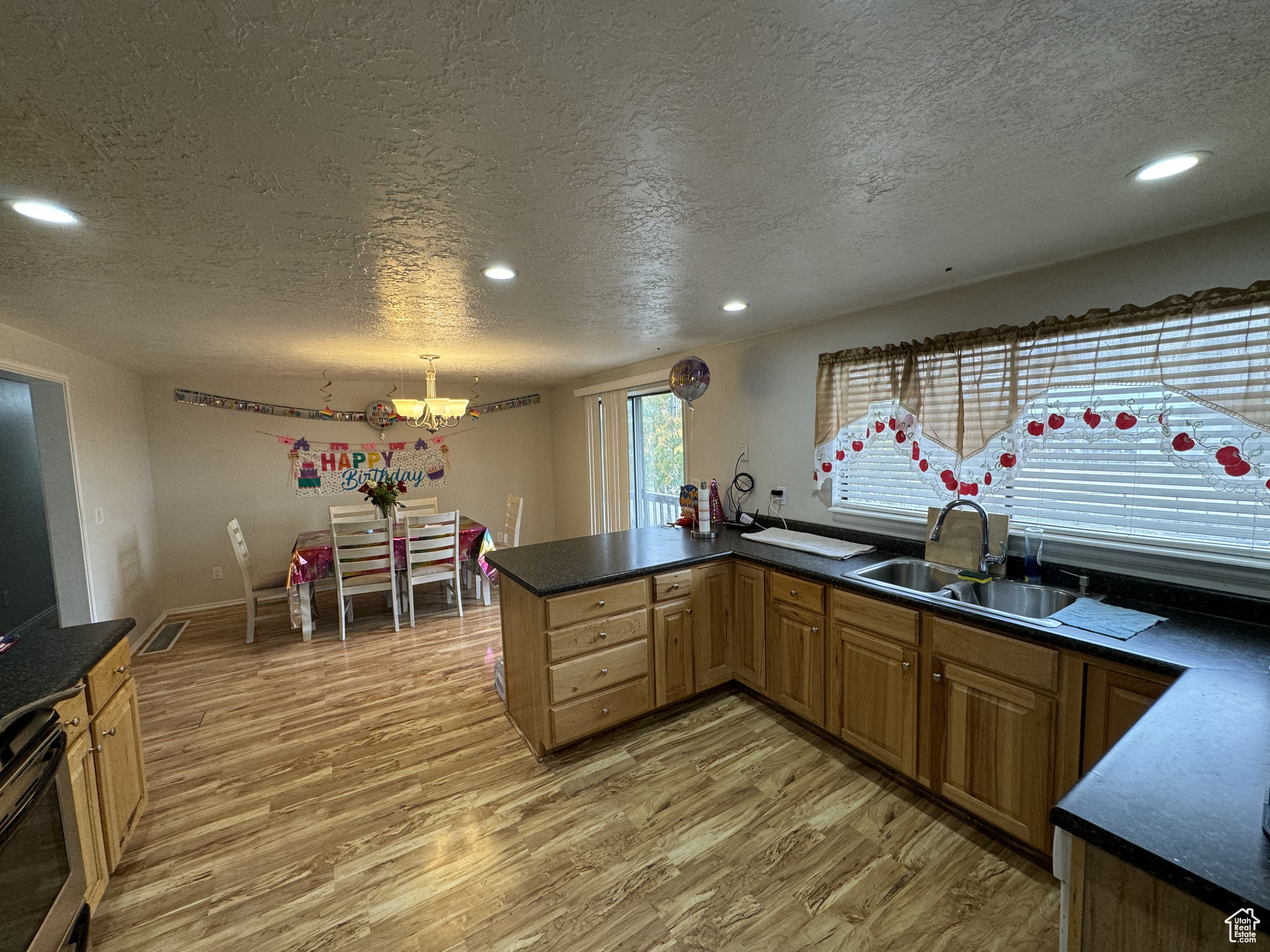 Kitchen with wood-type flooring, a textured ceiling, pendant lighting, sink, and kitchen peninsula