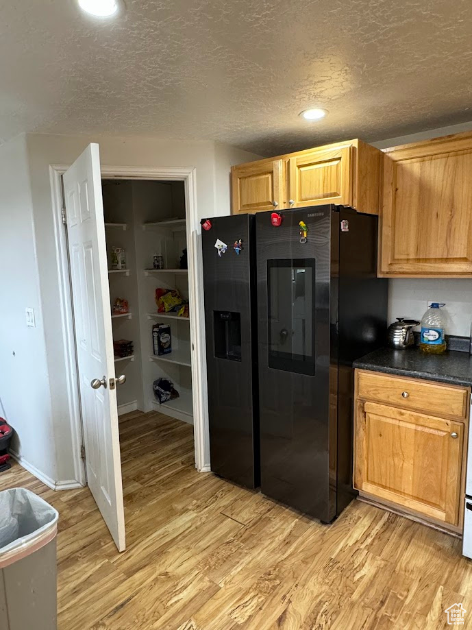 Kitchen with dark countertops, light wood-style flooring, refrigerator with ice dispenser, and a textured ceiling