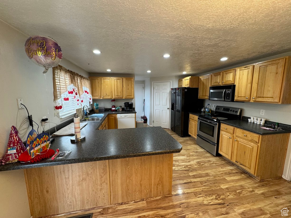 Kitchen featuring a textured ceiling, dark countertops, recessed lighting, stainless steel appliances, and light wood finished floors