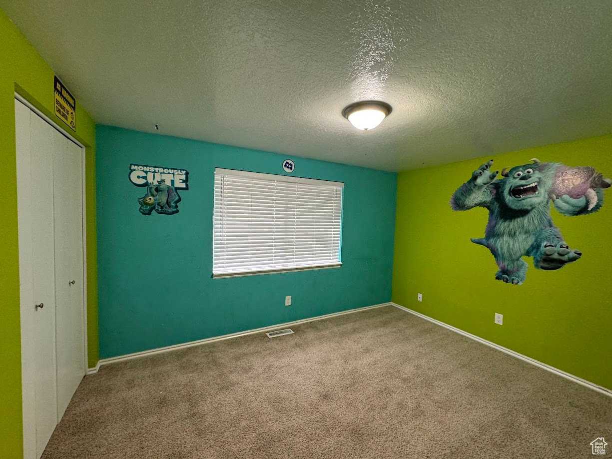 Carpeted empty room with visible vents, a textured ceiling, and baseboards