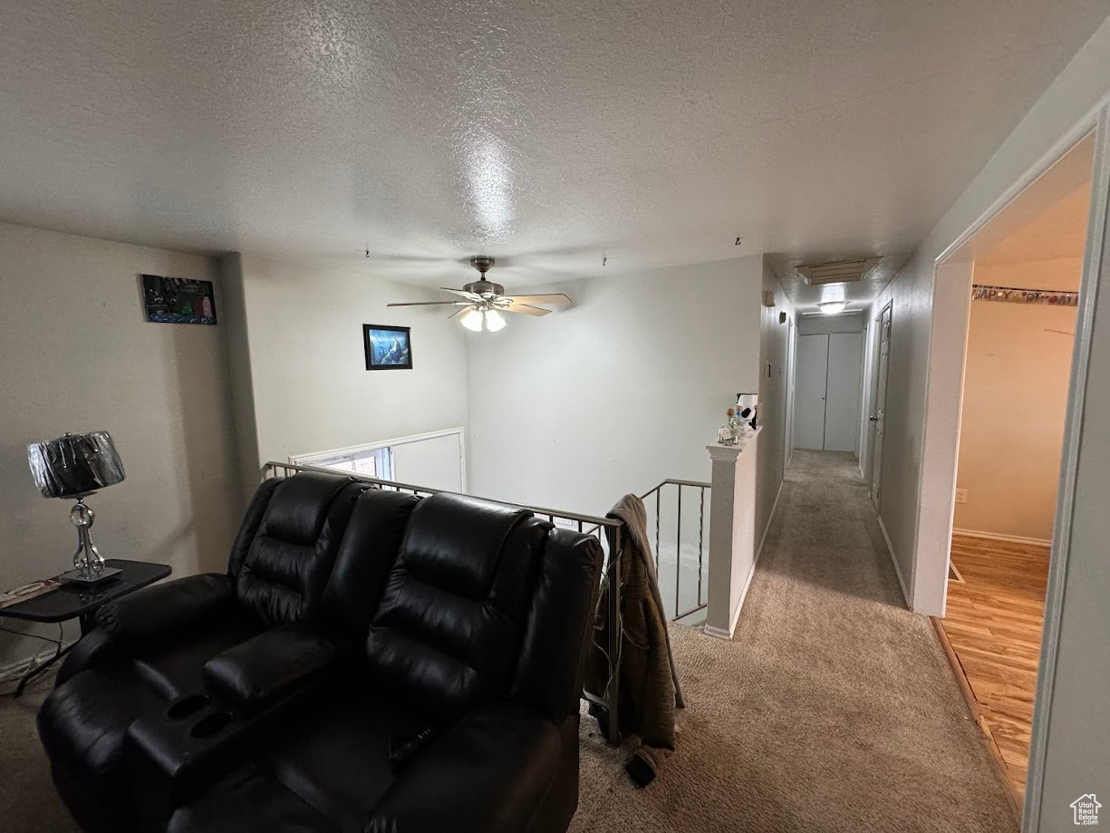 Living area with a ceiling fan, light colored carpet, and a textured ceiling