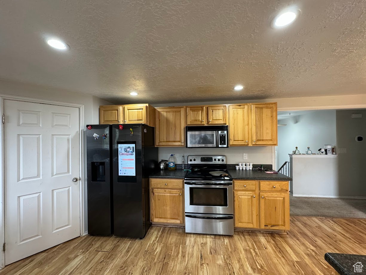 Kitchen featuring dark countertops, recessed lighting, stainless steel appliances, light wood-style floors, and a textured ceiling