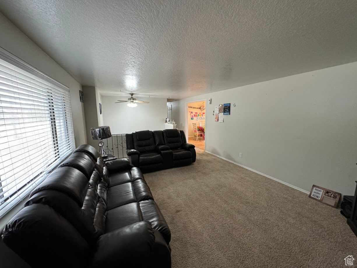 Carpeted living room featuring baseboards, a textured ceiling, and a ceiling fan