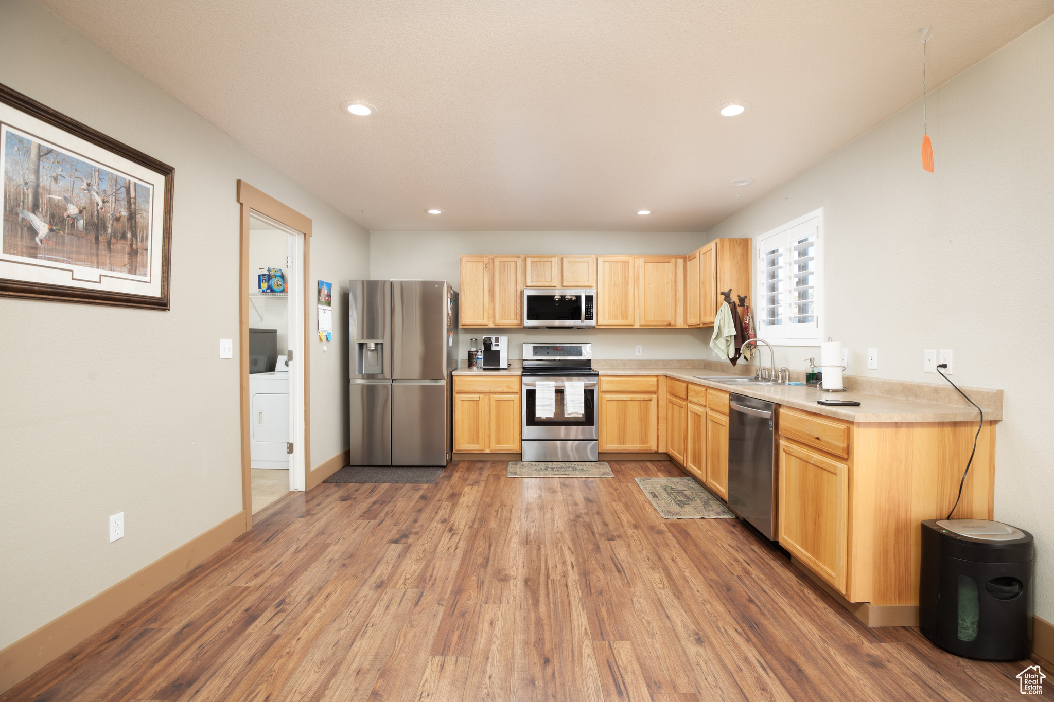 Kitchen featuring hardwood / wood-style flooring, sink, light brown cabinets, appliances with stainless steel finishes, and washer / clothes dryer