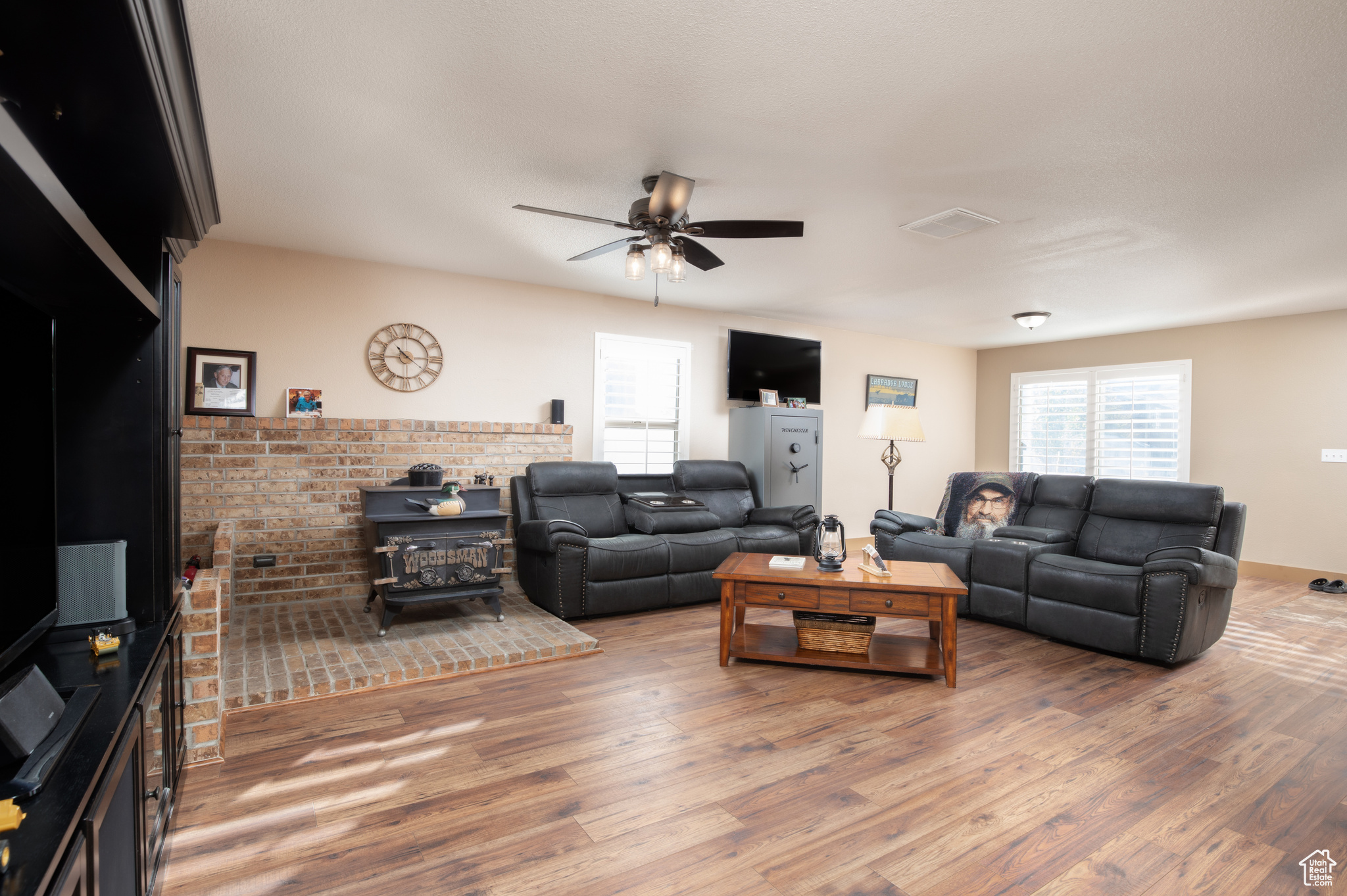 Living room with a wood stove, wood-type flooring, and ceiling fan