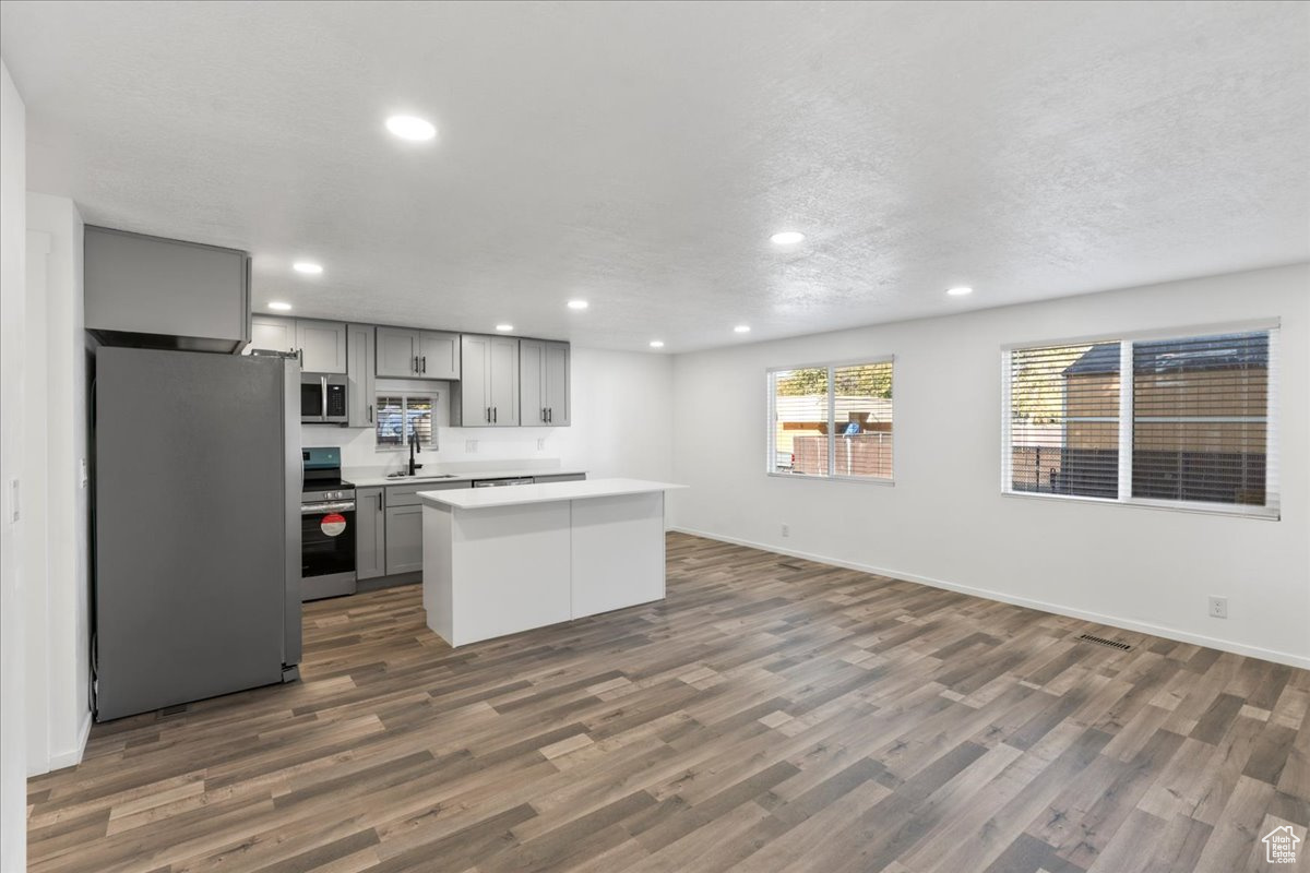 Kitchen with dark hardwood / wood-style flooring, sink, gray cabinetry, a kitchen island, and appliances with stainless steel finishes