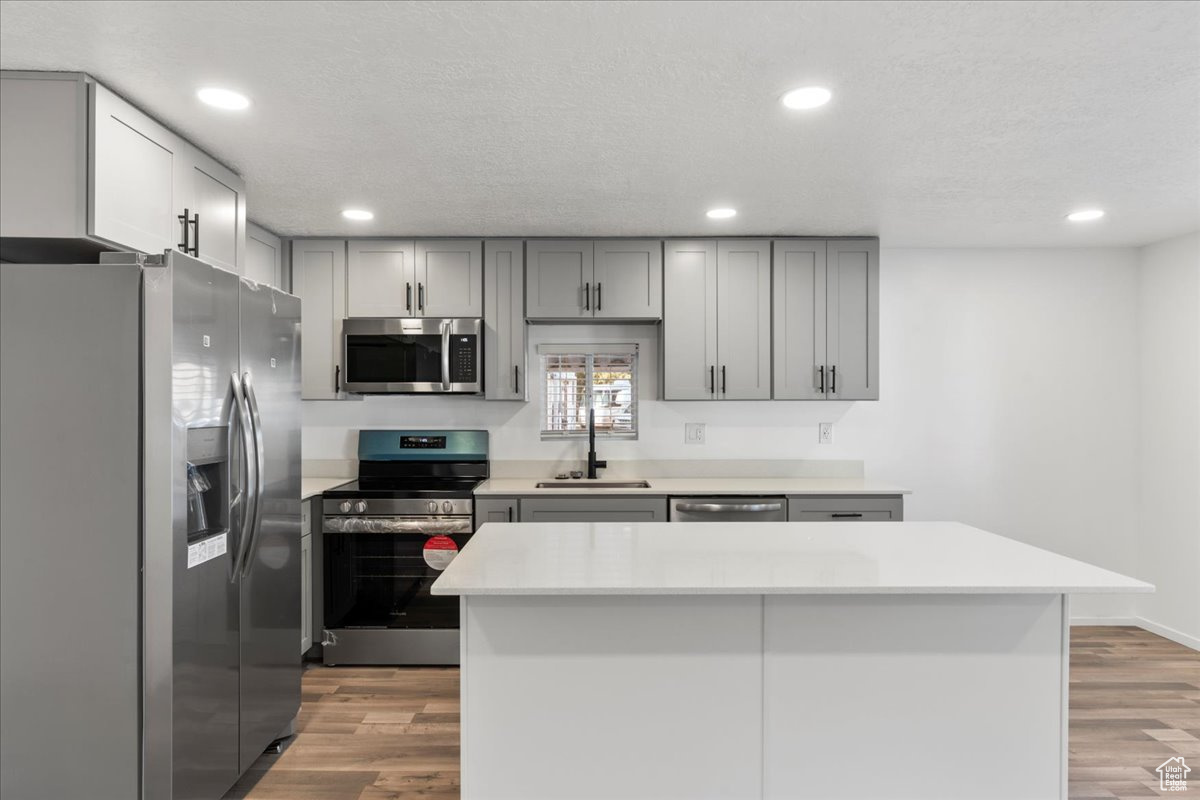 Kitchen featuring stainless steel appliances, hardwood / wood-style floors, sink, gray cabinets, and a kitchen island