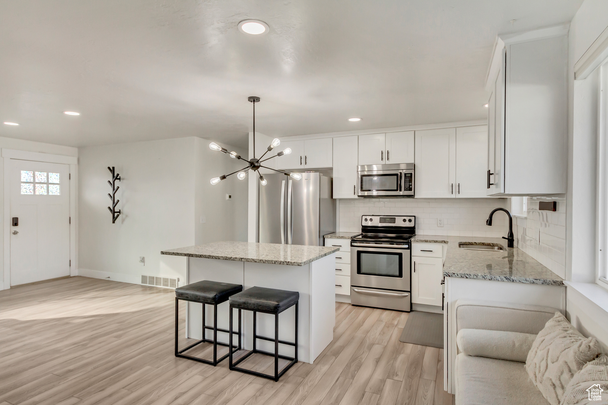 Kitchen featuring white cabinetry, a center island, sink, stainless steel appliances, and light wood-type flooring