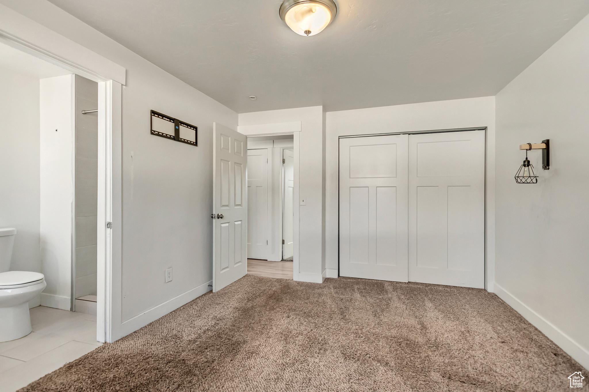 Unfurnished bedroom featuring light colored carpet, connected bathroom, and a closet