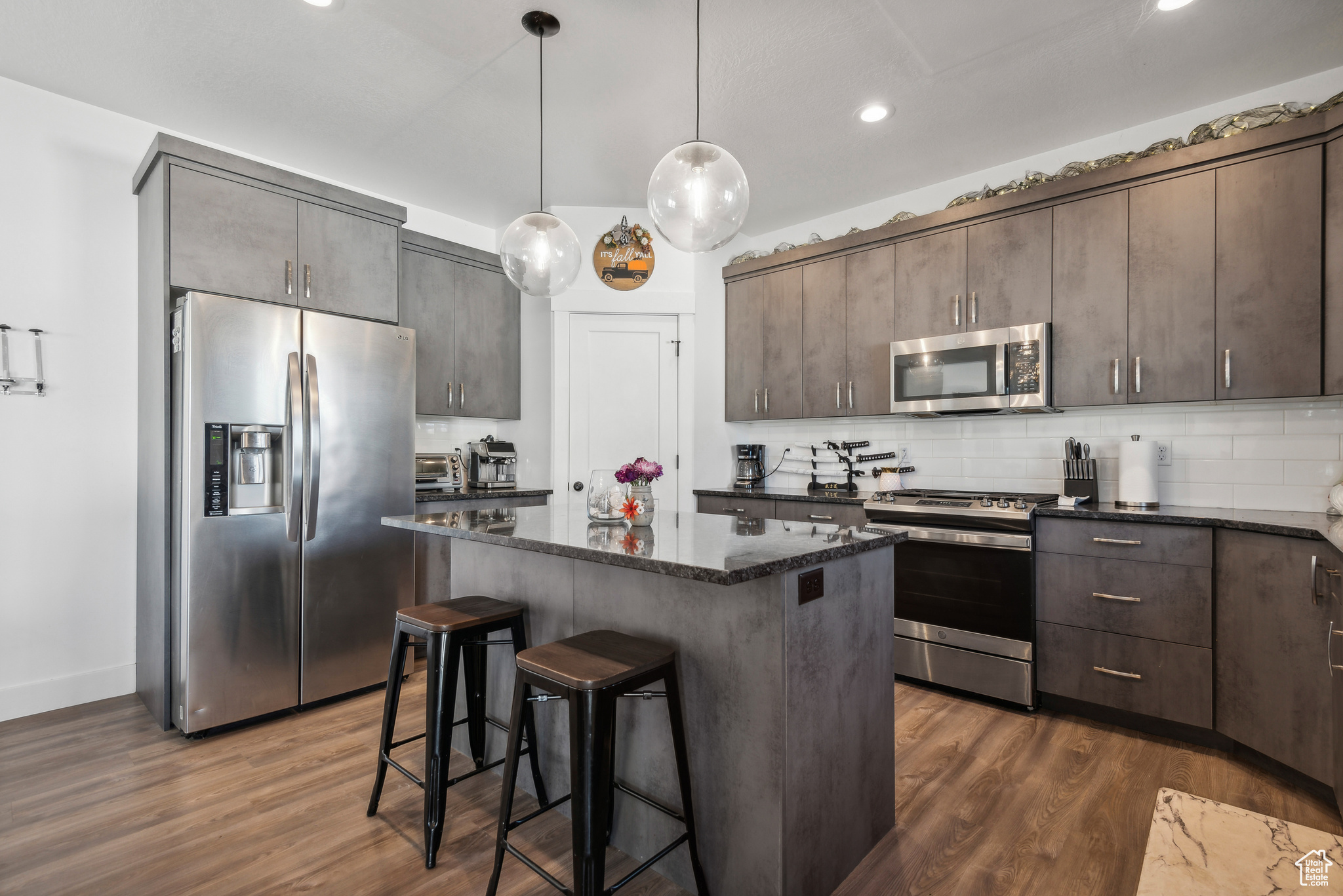 Kitchen with tasteful backsplash, dark stone counters, appliances with stainless steel finishes, dark brown cabinetry, and dark hardwood / wood-style flooring