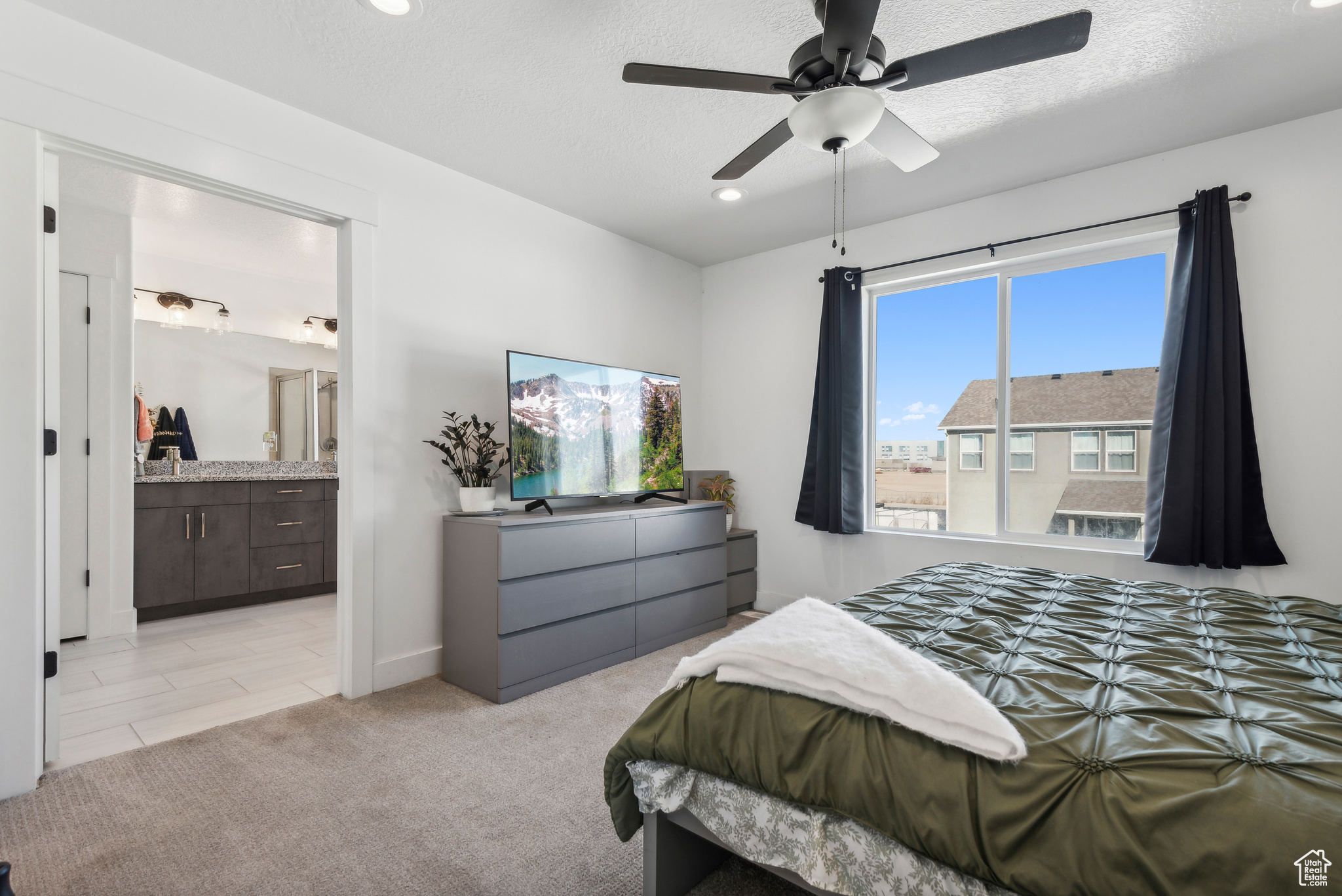 Carpeted bedroom with connected bathroom, a textured ceiling, and ceiling fan