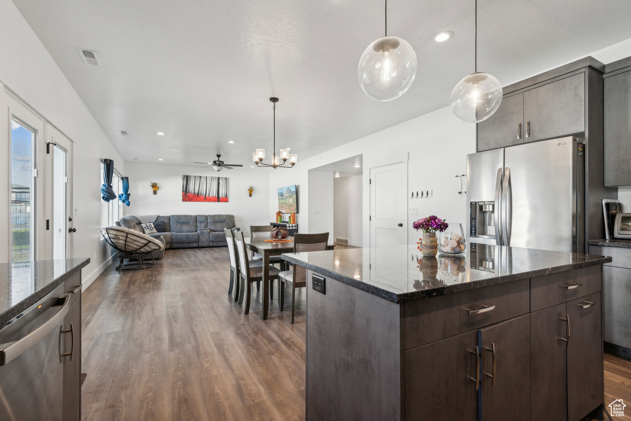 Kitchen with appliances with stainless steel finishes, dark brown cabinets, a center island, pendant lighting, and dark hardwood / wood-style flooring