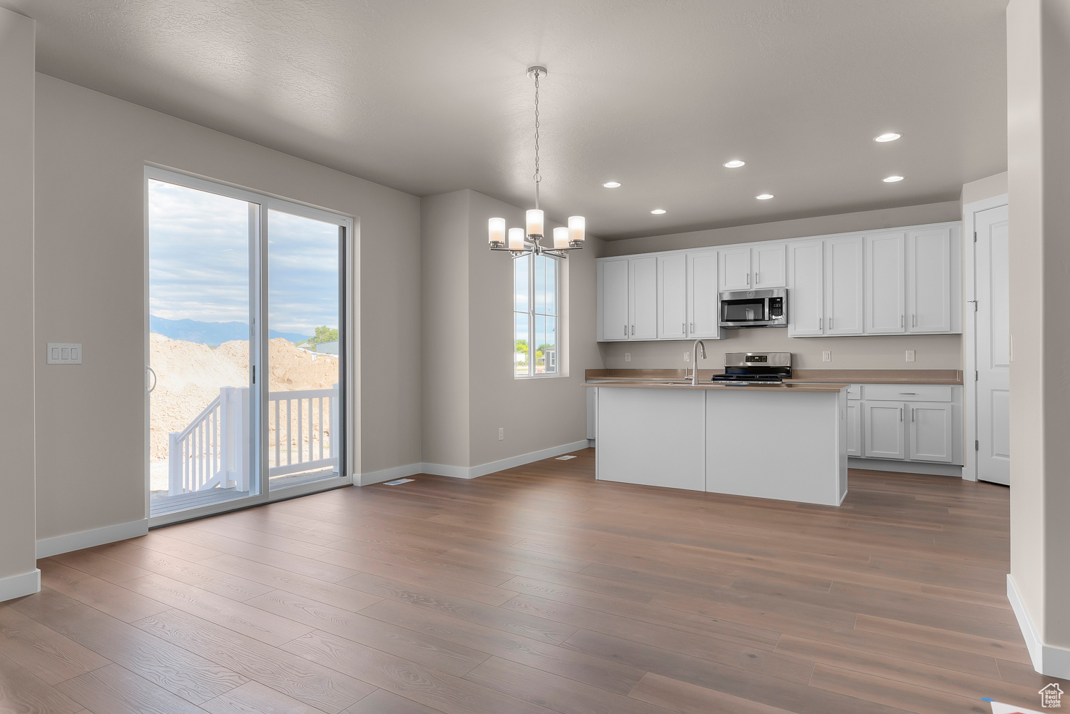 Kitchen with stainless steel appliances, white cabinetry, a center island with sink, decorative light fixtures, and hardwood / wood-style floors