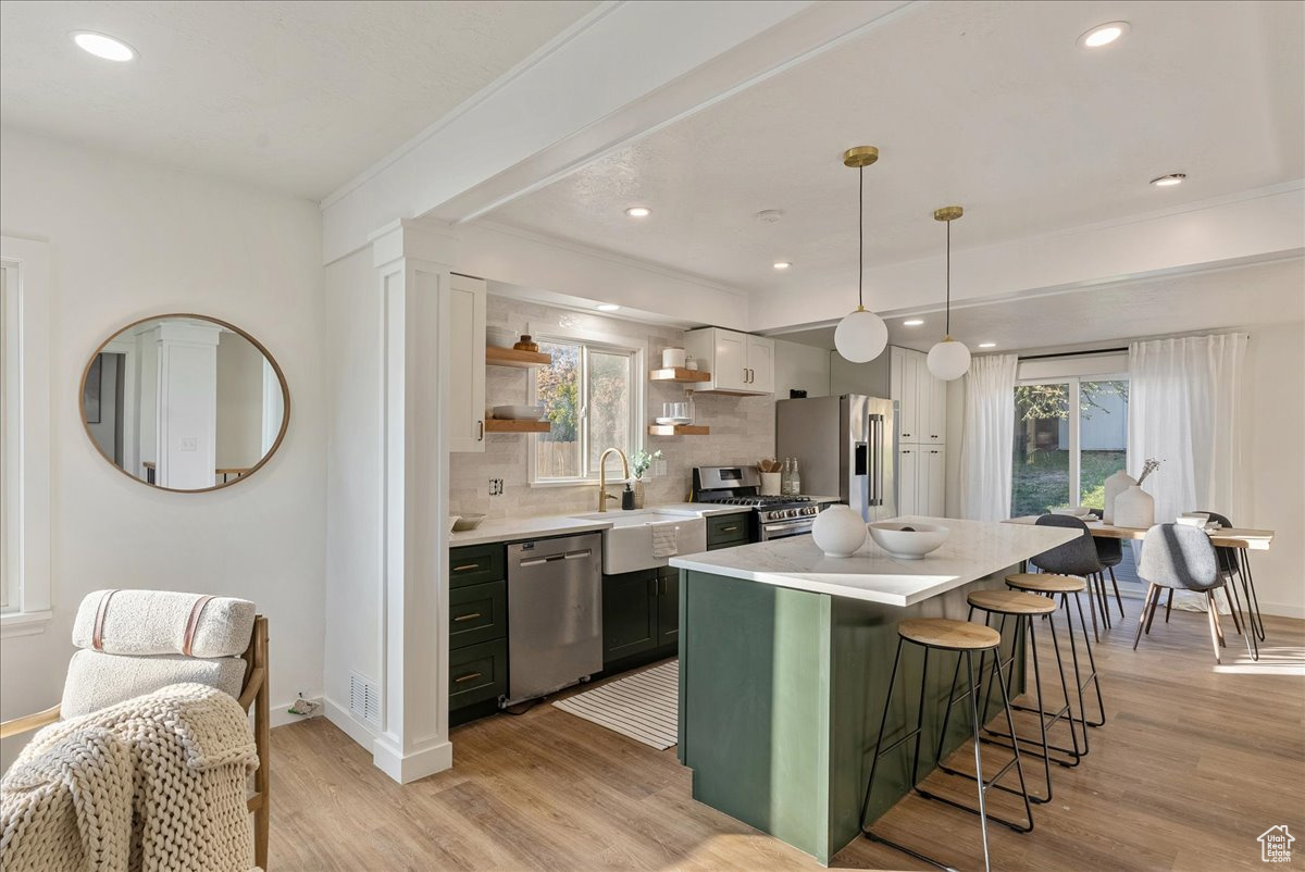 Kitchen featuring appliances with stainless steel finishes, decorative light fixtures, decorative backsplash, white cabinets, and light hardwood / wood-style flooring