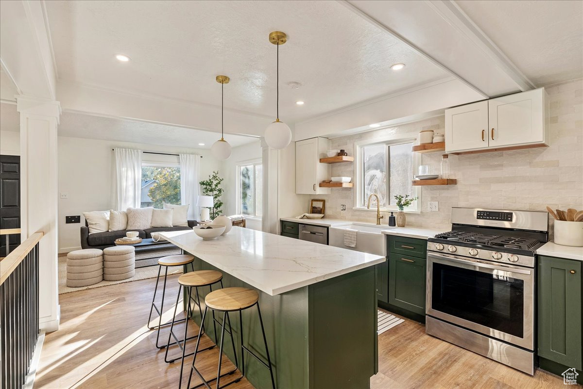 Kitchen with stainless steel range with gas cooktop, green cabinetry, light hardwood / wood-style flooring, white cabinets, and decorative backsplash