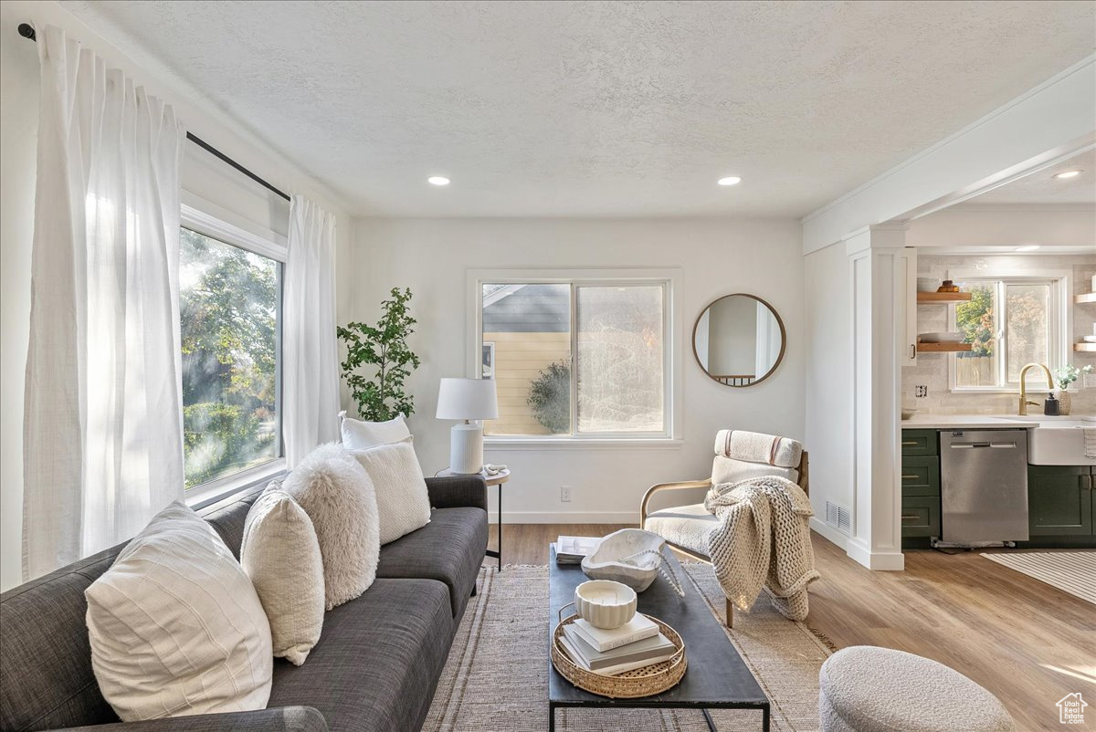 Living room featuring sink, decorative columns, a textured ceiling, and light hardwood / wood-style flooring