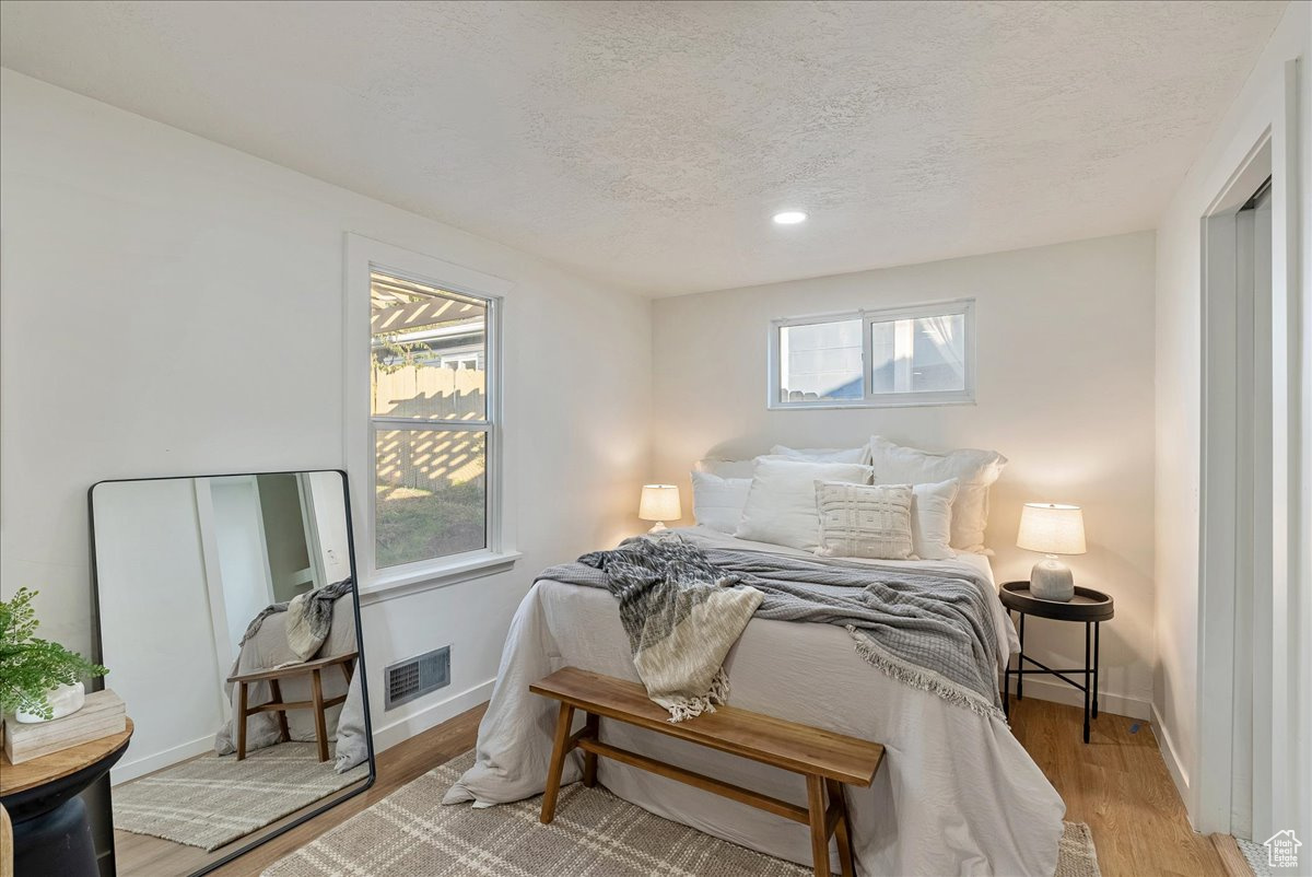 Bedroom with light wood-type flooring, multiple windows, and a textured ceiling