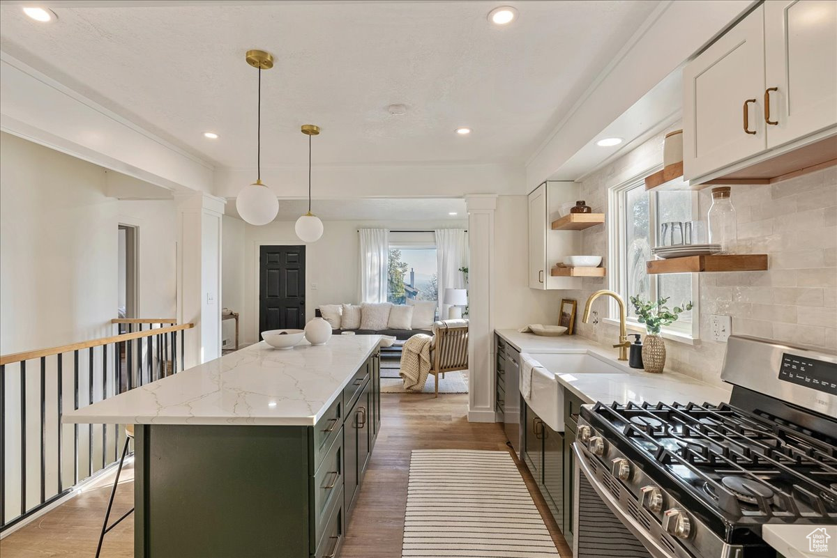 Kitchen with stainless steel range with gas cooktop, white cabinetry, light stone countertops, decorative light fixtures, and dark wood-type flooring